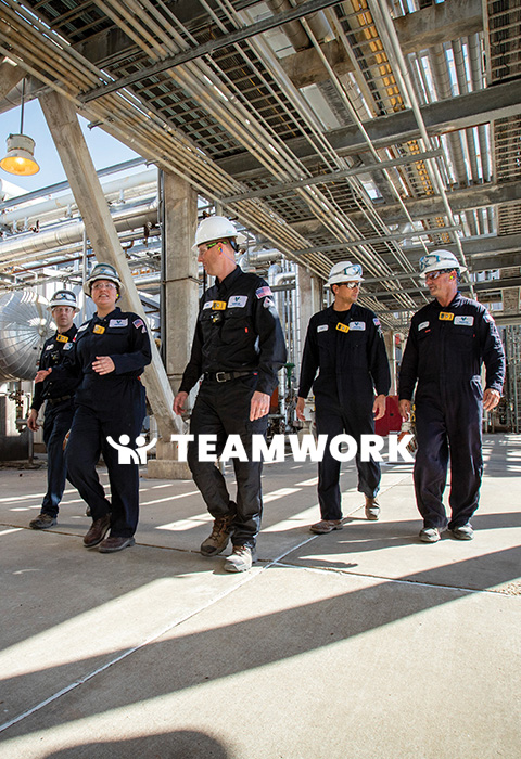 Valero employees wearing full PPE walk together at a refinery. Text reads: Teamwork.